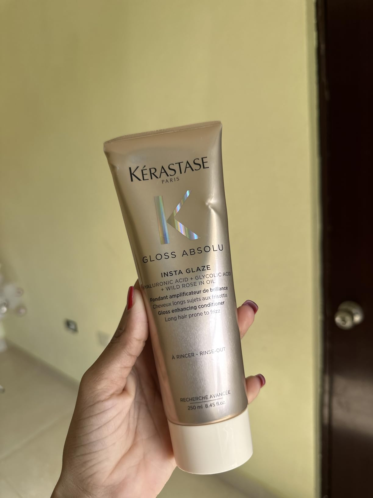 Person holding a vessel  of Kérastase Gloss Absolu Insta Glaze hairsbreadth  merchandise  indoors
