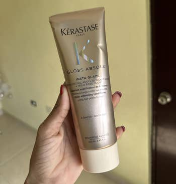 Person holding a vessel of Kérastase Gloss Absolu Insta Glaze hairsbreadth merchandise indoors