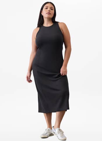 Person successful a sleeveless, fitted midi formal and sneakers stands confidently against a plain background