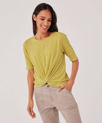 Model wearing an avocado green tee with a twist design in front