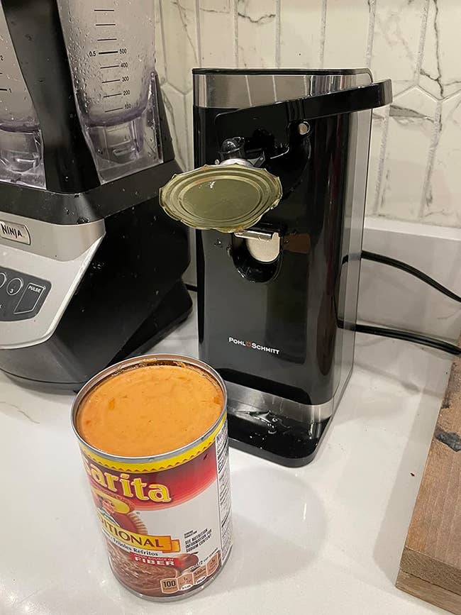 A reviewer's can opener with an open can on the counter and the lid still attached to the opener