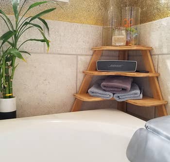 reviewer's three-tier shelf in the corner of tub area holding bath supplies
