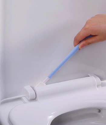 model using a blue crevice cleaning tool on a toilet