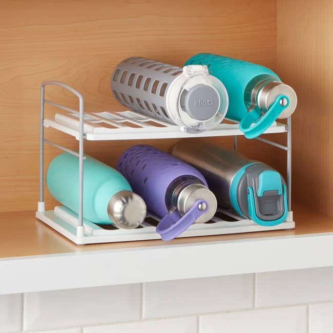 Water bottle organizer holding various reusable bottles on a white shelf in a kitchen setting