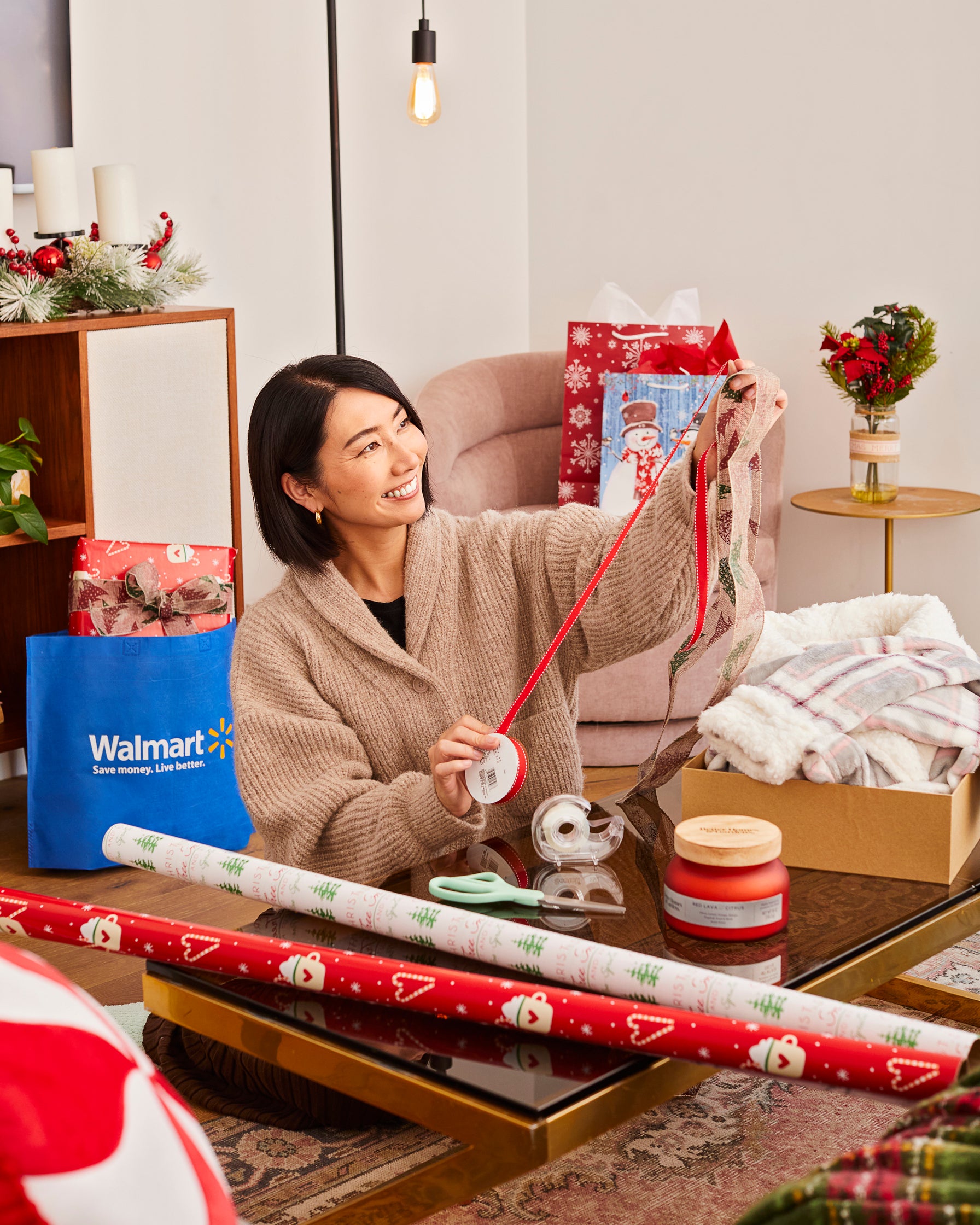 Rie holds up ribbon above table with scissors, tape, wrapping paper, and candle on it