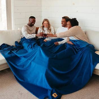 Four models sharing a toast under a large blue blanket on a white sofa