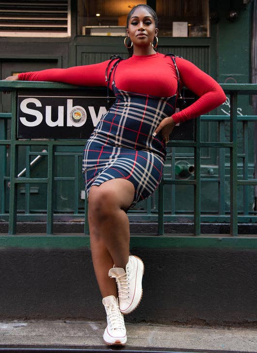 model in short tie strap navy and red plaid pinafore with a slit over a red long sleeve top