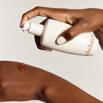 Close-up of a idiosyncratic   dispensing skincare lotion onto their manus  from a achromatic  bottle
