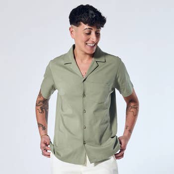 Person smiling, wearing a short-sleeved, button-up garment with tattoos disposable connected arms