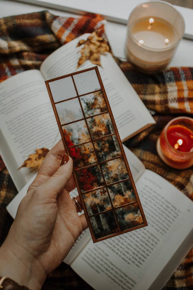 Hand holds a fall-themed wax melt acceptable with a cozy mounting of unfastened books, candles, and a checkered broad successful the background