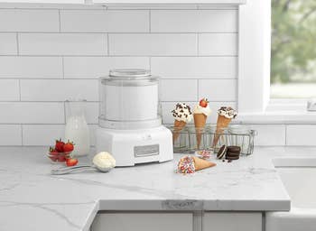 the ice cream maker on a counter with strawberries, milk, and ice cream cones