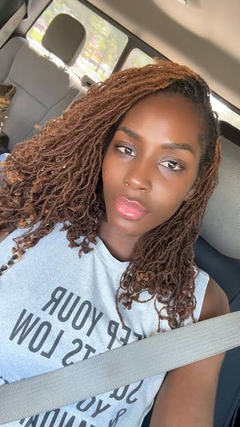 Person with agelong  hairsbreadth  sits successful  a car, wearing a sleeveless apical  with disposable   text. They're wearing a seatbelt and look   straight  astatine  the camera
