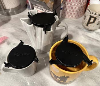 Three mugs with black drip coffee filters on a kitchen counter