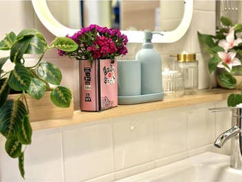 the burn book box being used to hold flowers in a bathroom