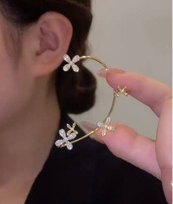 Model holding a gold ear cuff with sparkly flowers on it 