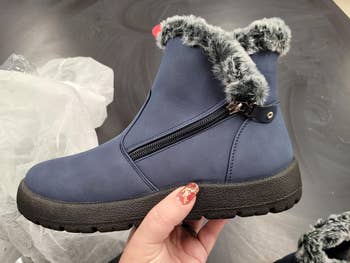 A idiosyncratic   holding a wintertime  footwear  with a faux fur trim and broadside  zipper, suitable for acold  weather. The footwear  is shown against a acheronian  background