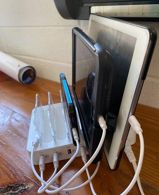 a reviewer photo of the charging station charging a phone and two tablets with empty slots to spare 