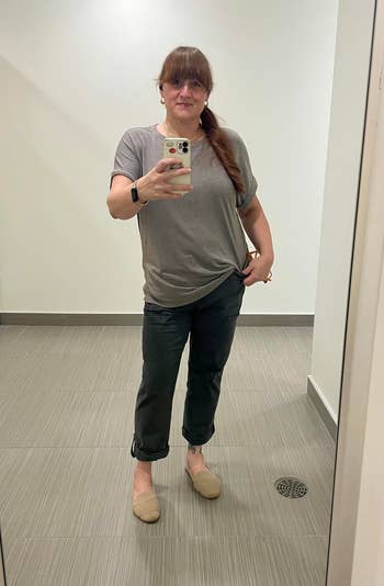 Person successful  casual outfit with a grey  T-shirt, acheronian  pants, and beige shoes, taking a reflector  selfie successful  a minimalist room