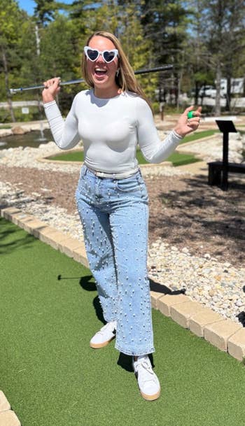 Person successful high-waist jeans and long-sleeve apical playfully poses connected mini-golf people