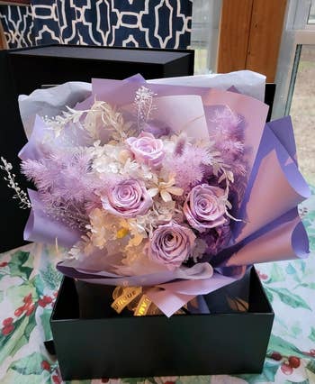 A bouquet of mixed flowers in various shades, presented in a black gift box