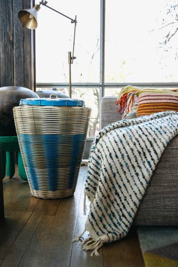 Wicker laundry basket next to a couch with a striped blanket in a cozy room setting