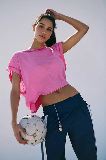 Person in casual sportswear holding a soccer ball, wearing a loose top and athletic pants. Perfect for an active, sporty fashion look
