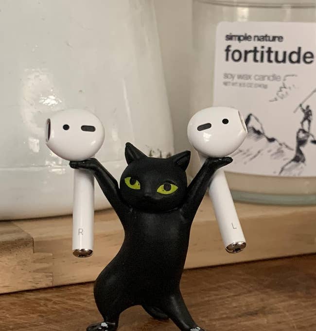 black cat figurine standing on hind legs and holding an airpod on each paw