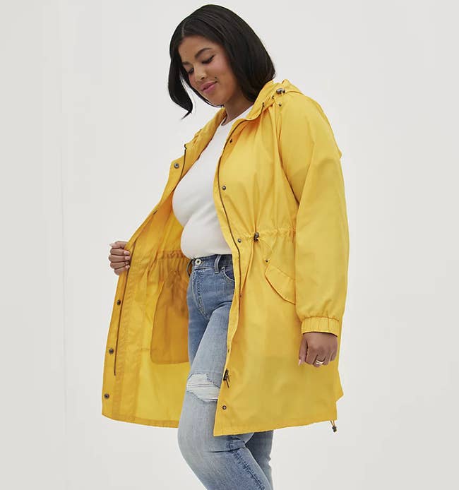 Model is wearing a white top, denim jeans, and a yellow rain coat