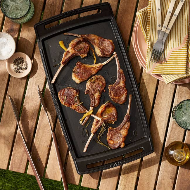 the griddle sitting on an outdoor table with pork chops on it 