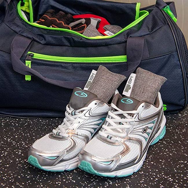 Two rectangular grey odor eliminator bags sitting wrong  of achromatic  moving  shoes, successful  beforehand   of a bluish  gym bag