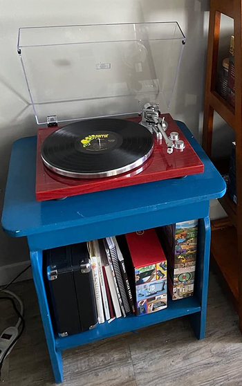 Reviewer image of red and clear turntable with two silver dials and a silver needle sitting atop a light blue side table