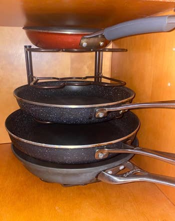 Various sized frying pans stacked on the organizer inside a kitchen cabinet