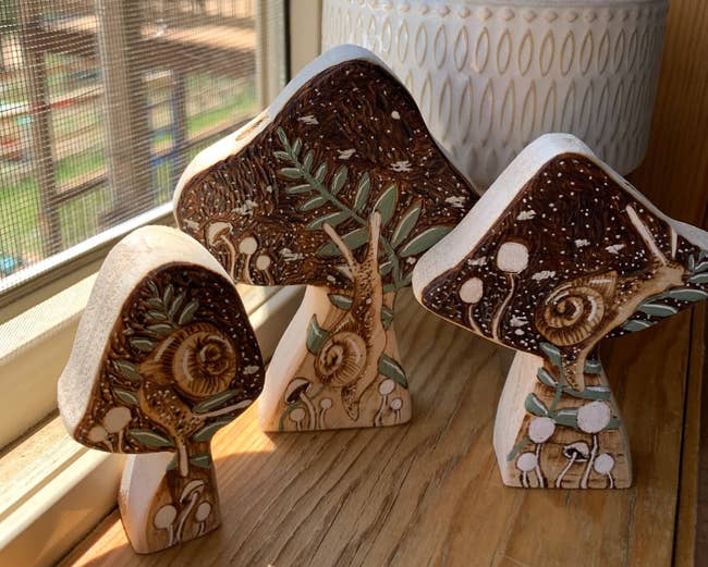 Three mushroom-shaped pieces of wood with snails and white mushrooms painted on them