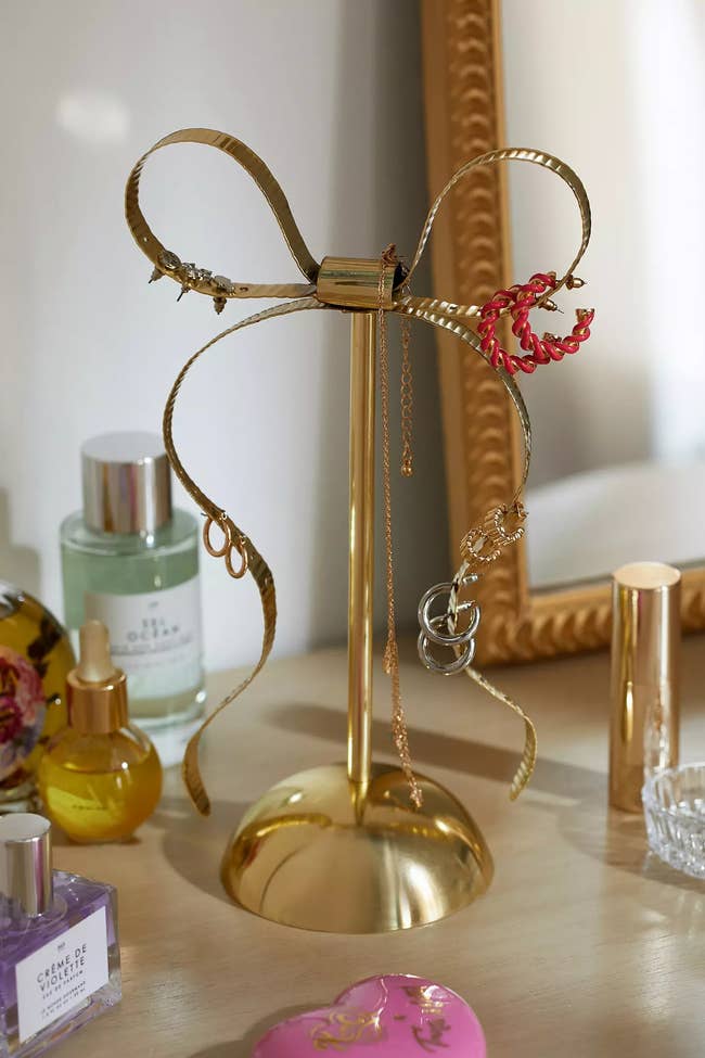 Decorative metal ribbon stand with a floral detail and a ring, placed on a dresser with cosmetics