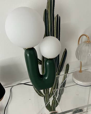 A unique two-bulb lamp with a white and green design, positioned next to a cactus, suggesting a modern home decor aesthetic