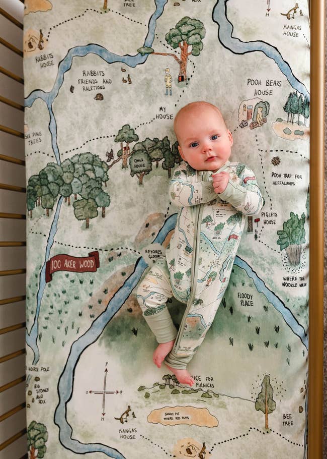 a baby lying on a crib mattress that looks like a map of hundred acre woods