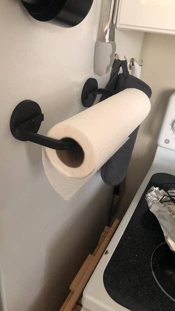 reviewer photo of the holder attached to the side of a fridge with a roll of paper towels on it