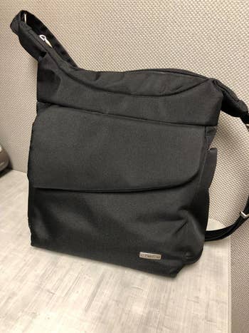 A reviewer's black messenger bag with a flap front and adjustable strap against a textured background