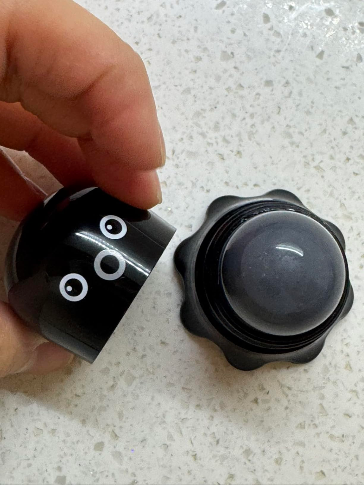 Hand opening   a cute achromatic  instrumentality  with circular  eyes, revealing a dome-shaped exfoliator inside