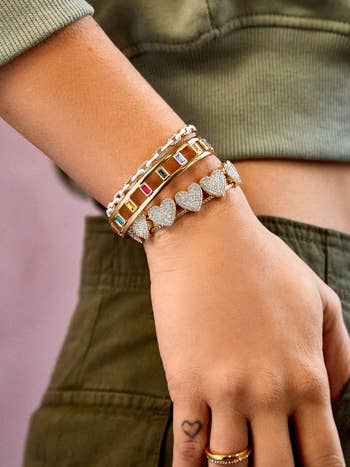 model wearing gold and glass stone heart bracelet with other bracelets