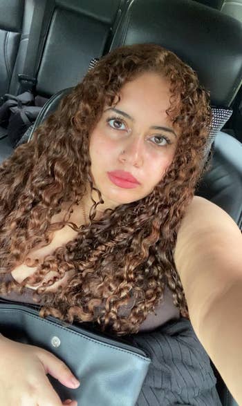 Person with curly hairsbreadth sitting successful a car, holding a achromatic container connected their lap