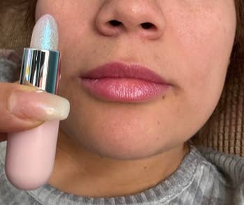 a reviewer holding a shimmery lip balm and showing off pink shimmery lips