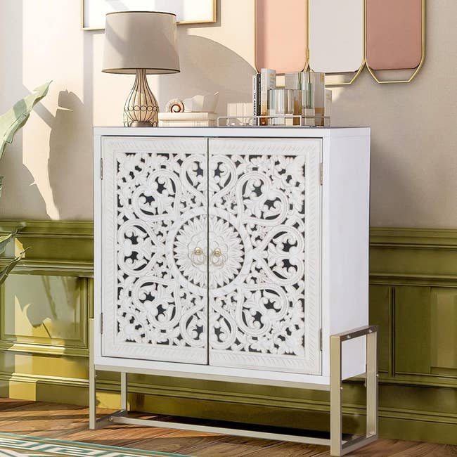 white storage cabinet on brass legs with two doors on the front