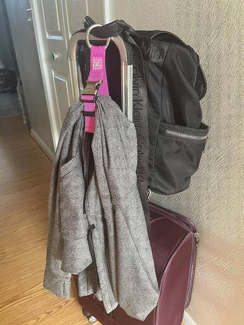 A achromatic  backpack and a grey  overgarment   are attached to a maroon suitcase successful  a hallway, with sunlight streaming successful  from the left