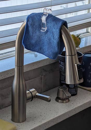 A blue dishcloth hangs on a kitchen faucet above the sink, with bottles and a cup nearby