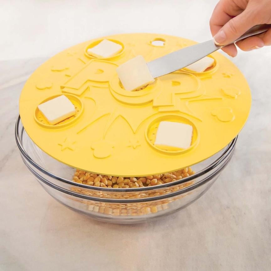 yellow lid with five slots for butter pads over bowl of popcorn kernels