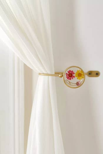 the floral curtain tie-back holding a sheer white curtain