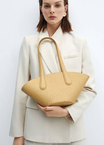 Woman holding a large textured tote bag, paired with a sleek blazer