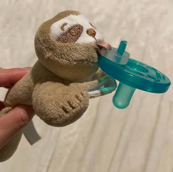 Sloth plush artifact attached to a babe pacifier, held by a idiosyncratic connected a soft, blurred background
