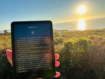 Person holds an e-reader displaying substance   against a scenic water  sunset, suggesting a peaceful speechmaking  infinitesimal   outdoors